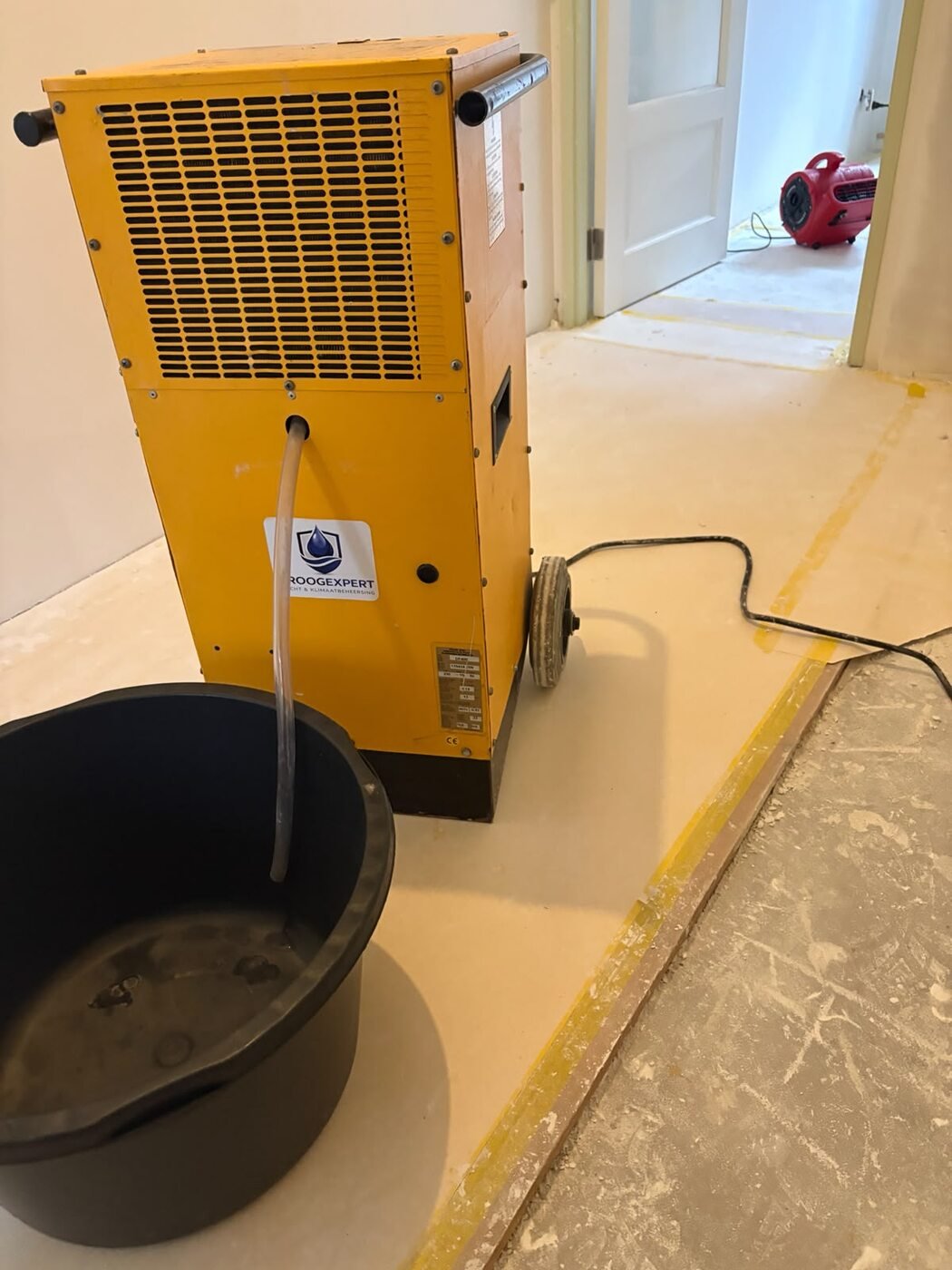 Professionele bouwdroger met condensafvoer en ventilator tijdens een bouwproject